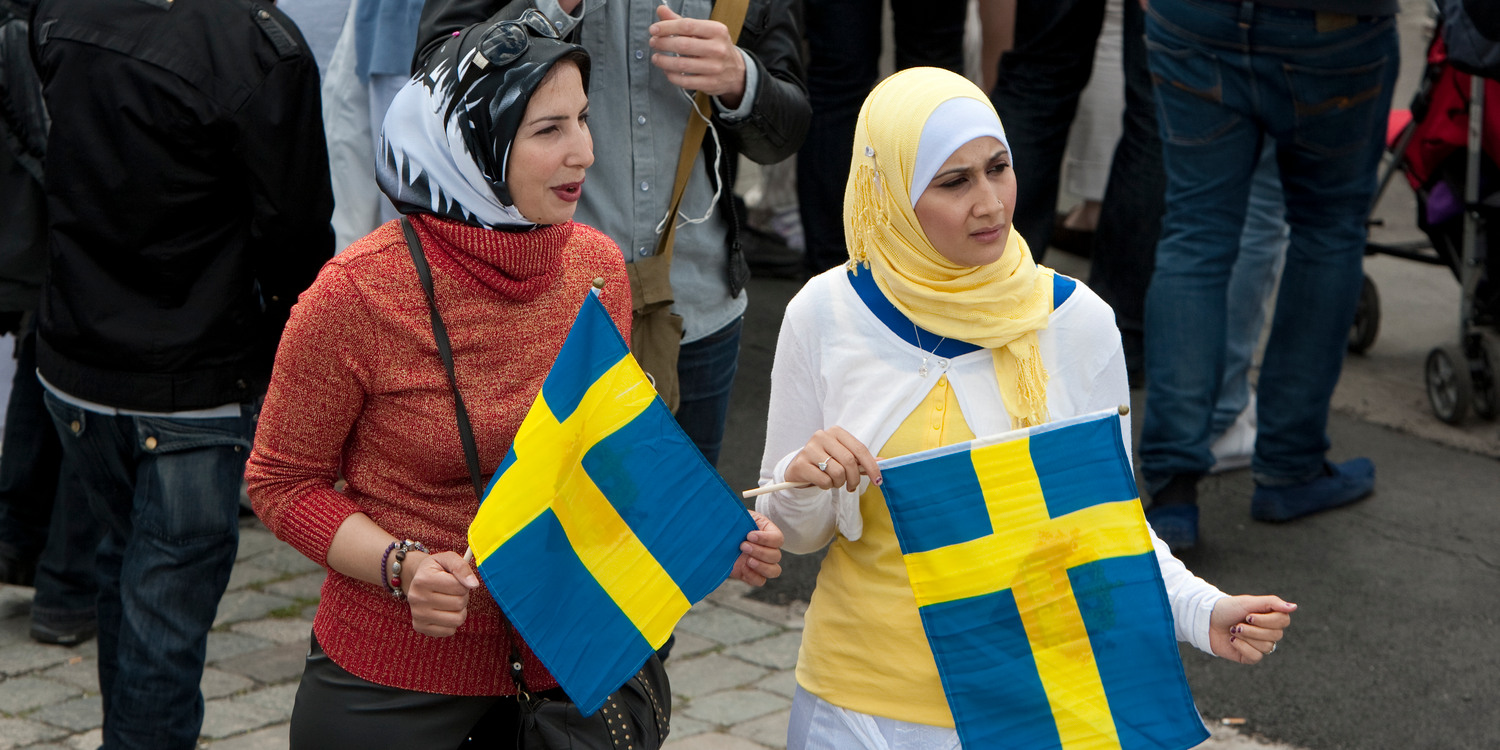 Två kvinnor i en folksamling. De har varsin svensk flagga i handen, som de viftar med.