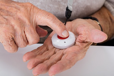 En larmknapp ligger i handflatan och personen trycker på knappen med pekfingret