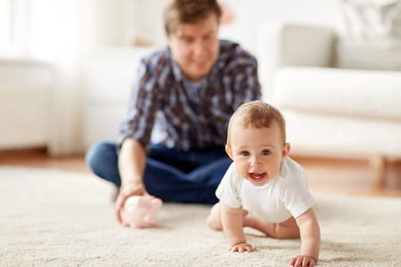 Ett barn kryper på mattan, pappan sitter i bakgrunden
