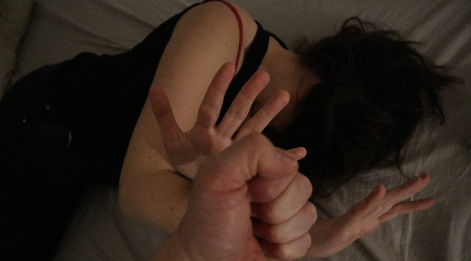 En kvinna ligger och värjer sig med en hand mot en knuten näve