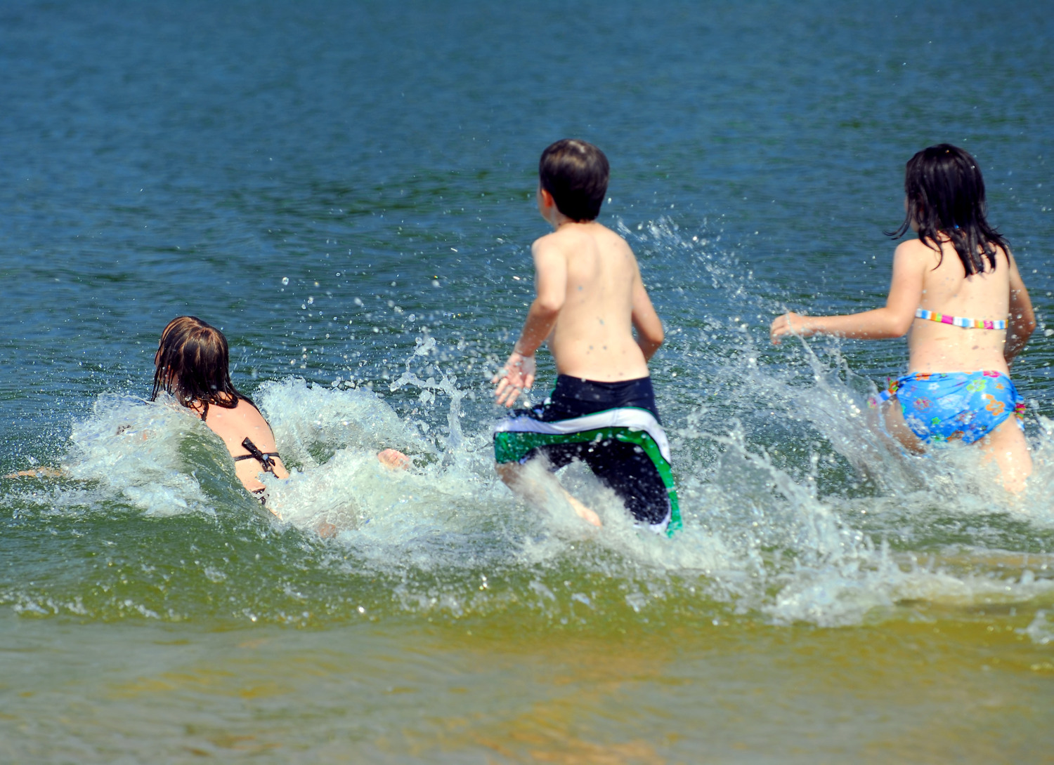 Tre barn som springer ut i vattnet 