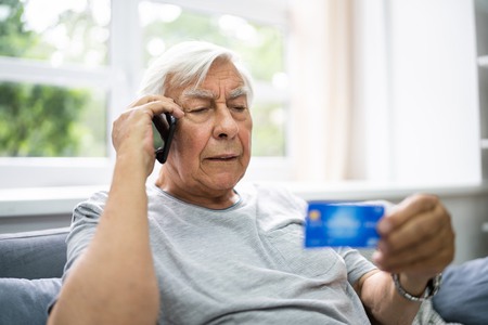 Äldre man som talar i telefon och håller i ett kreditkort