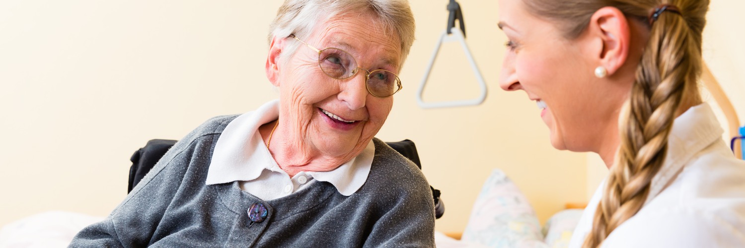 Två personer, en äldre och en yngre kvinna ler mot varandra