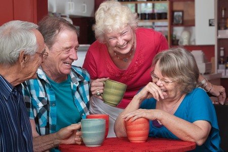 Ett gäng glada seniorer samlade runt ett bord med sina kaffemuggar